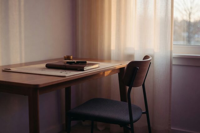 A desk with a notebook and fountain pen by a curtained window, chair pushed back